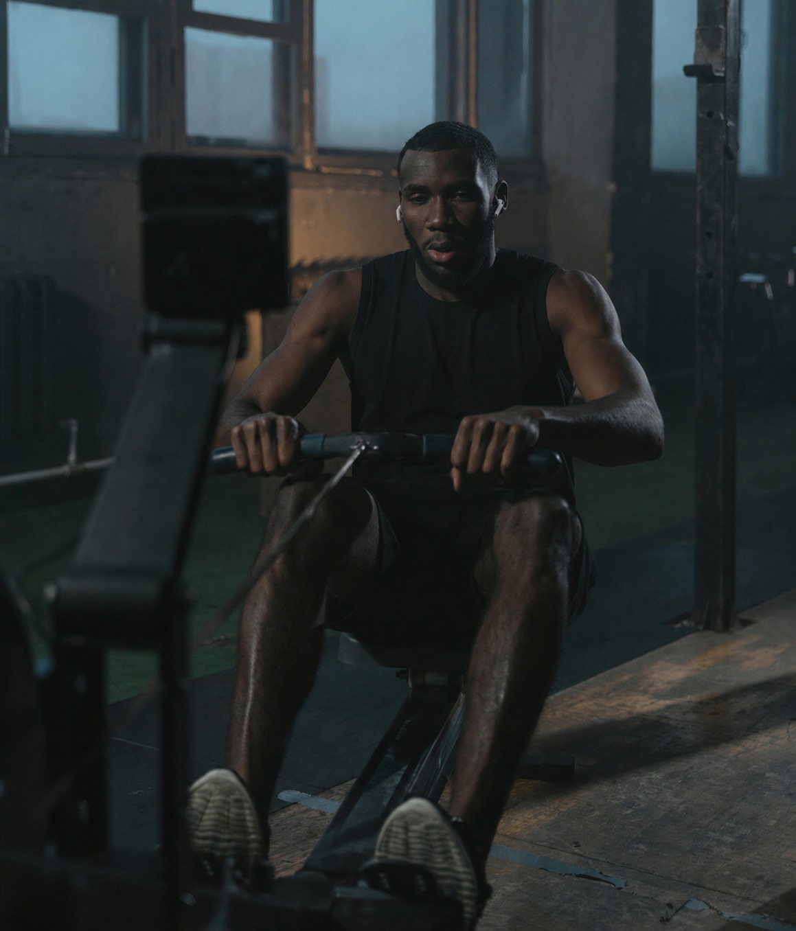 A person on a Concept2 ergometer wearing AirPods Pro, with live heart rate on the PM5