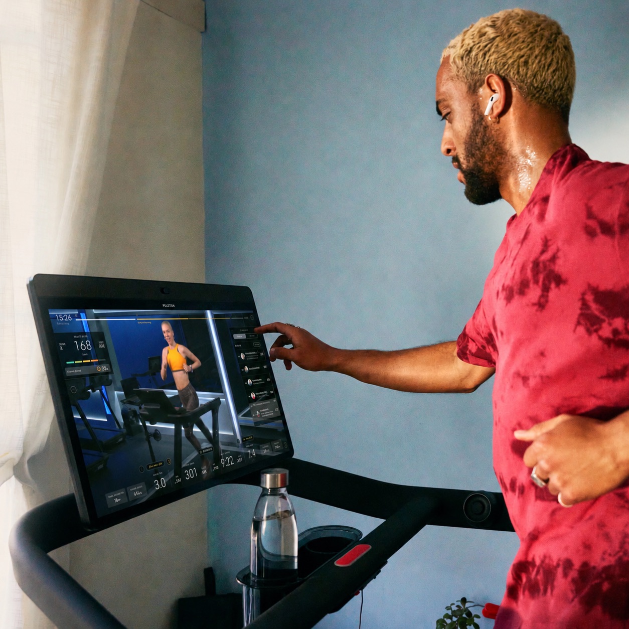 A person on a Peloton Bike wearing AirPods Pro, with live heart rate showing on the touchscreen